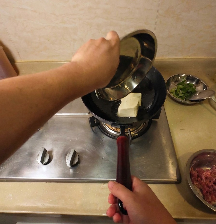 Un bloc entier de tofu blanc ajouté dans un wok dhuile chaude pour commencer la friture.