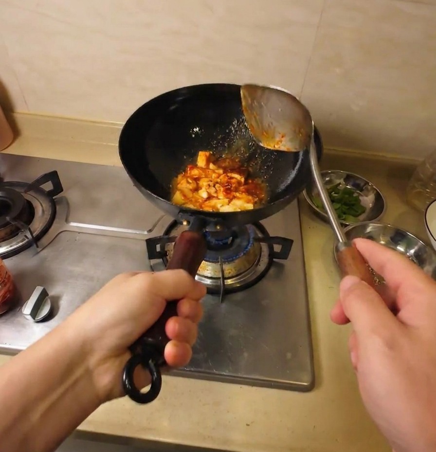 Morceaux de tofu sautés et enrobés dune sauce rouge savoureuse dans un wok noir.