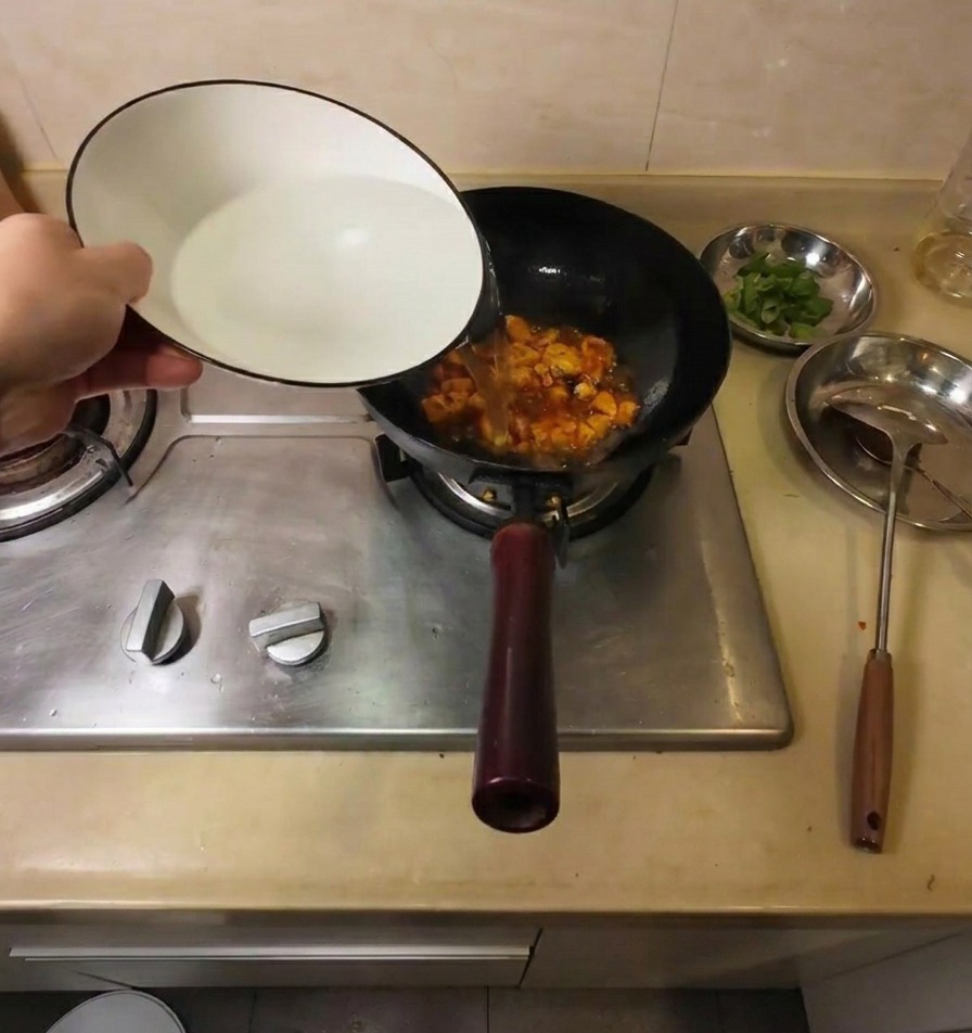 Eau chaude versée dun bol en céramique blanche dans un wok noir contenant du tofu frit et des assaisonnements rouges.