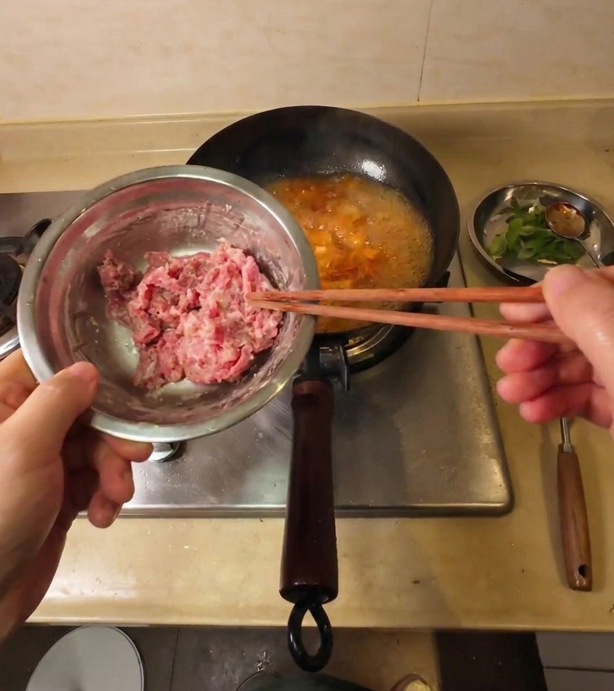 Une main utilisant des baguettes pour soulever des tranches de bœuf cru enrobées de fécule au-dessus dune soupe bouillonnante.