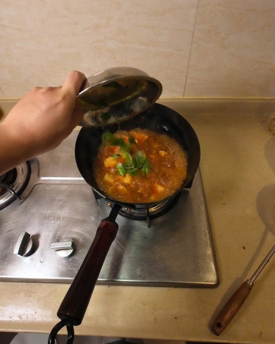 Une main versant des oignons verts frais hachés dun petit bol métallique dans un wok de soupe au bœuf et au tofu frémissante.