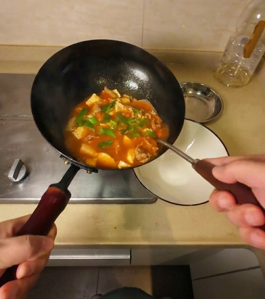 Soupe épaisse au bœuf et au tofu versée dun wok noir incliné dans un bol de service en céramique blanche.