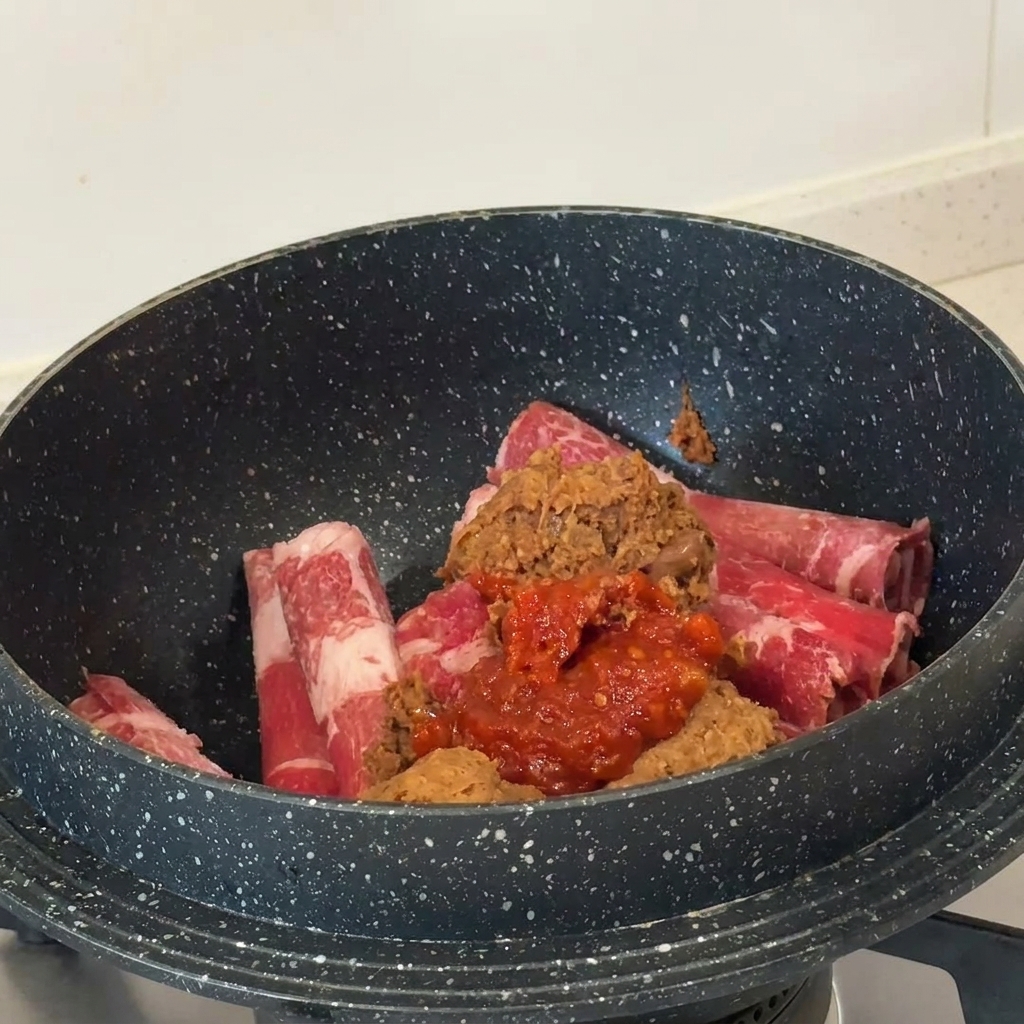Dômes de pâte de soja brune et de pâte de piment rouge sur la viande crue dans une casserole sombre.