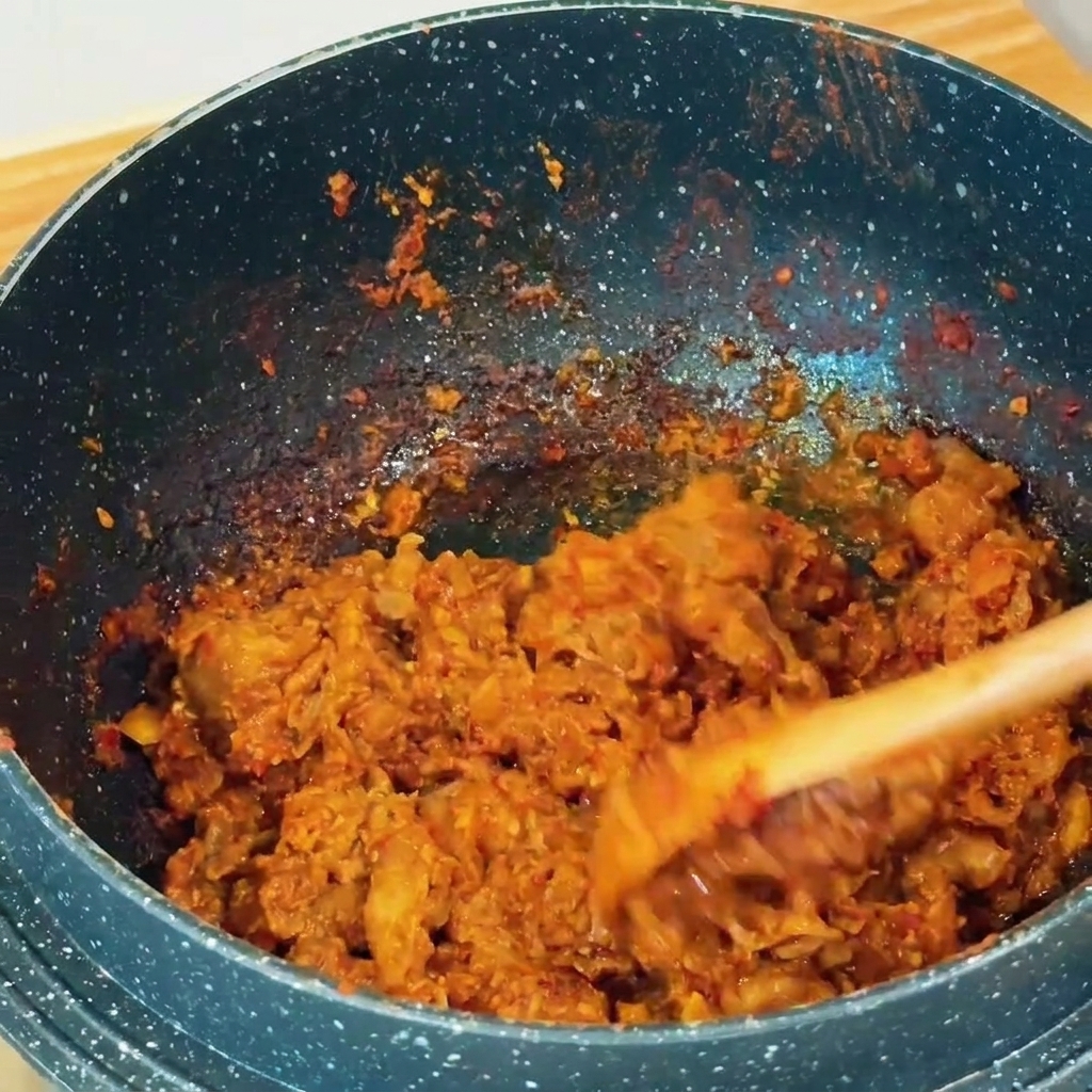 Fines tranches de bœuf sautées avec de la pâte de soja brun-rouge dans une casserole à laide dune spatule en bois.