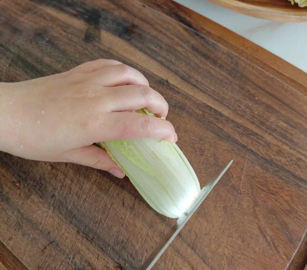 Un couteau de cuisine tranchant un petit chou frais sur une planche à découper en bois foncé.