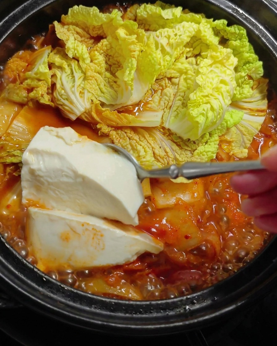 Une grande cuillerée de tofu blanc soyeux déposée délicatement dans un ragoût rouge chaud avec des feuilles de chou.