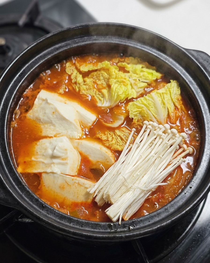 Bœuf tranché, champignons enoki et oignons verts ajoutés sur le dessus dun ragoût rouge bouillonnant.