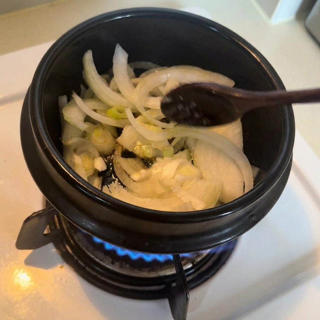 Oignons et oignons verts remués avec une cuillère en bois dans un pot en pierre noire sur le feu.