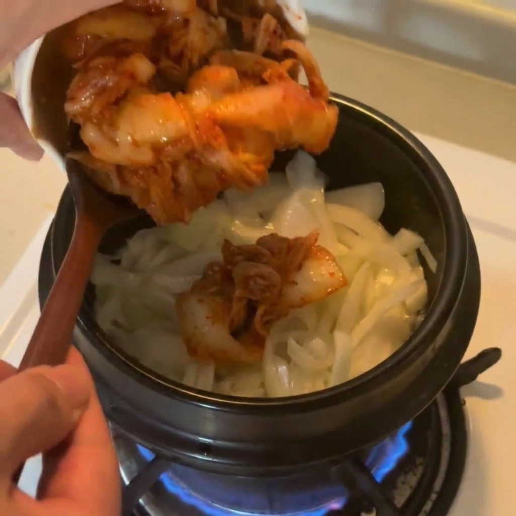 Kimchi haché versé dun bol en céramique blanche dans un pot doignons sautés.