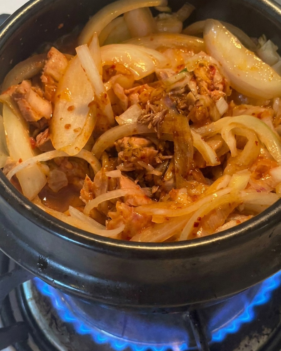 Gros plan de sauce soja brune versée sur le mélange de thon, kimchi et oignons dans un pot.