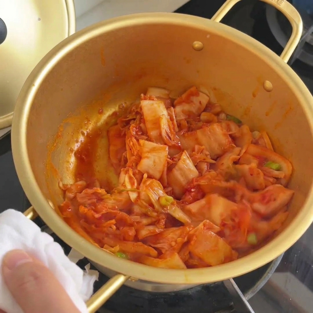 Kimchi et oignons verts sautés ensemble dans une marmite jusquà ce que le chou devienne translucide.