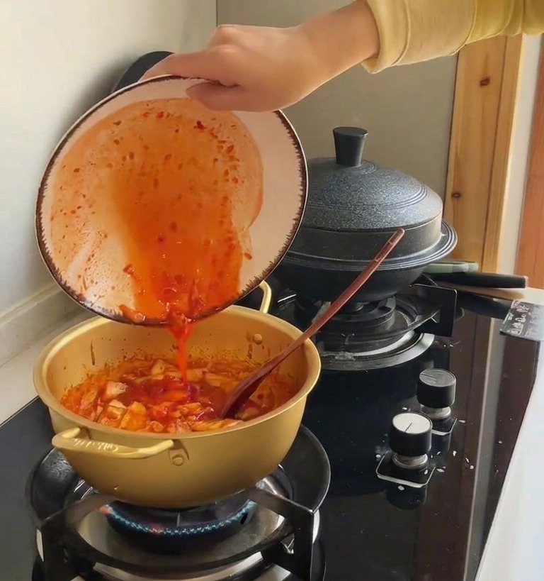 Jus de kimchi rouge vif versé dun bol en céramique dans une marmite remplie de chou sauté.