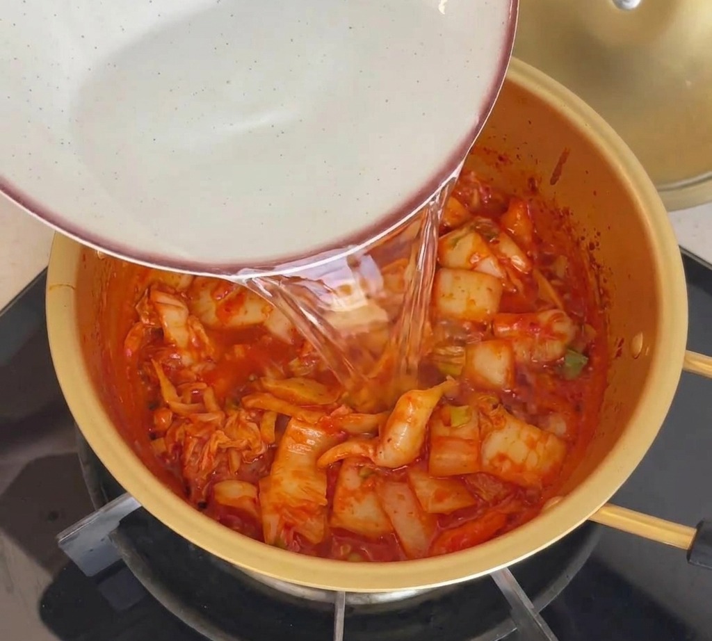 Eau versée dun bol en céramique dans une marmite dorée contenant le kimchi sauté.