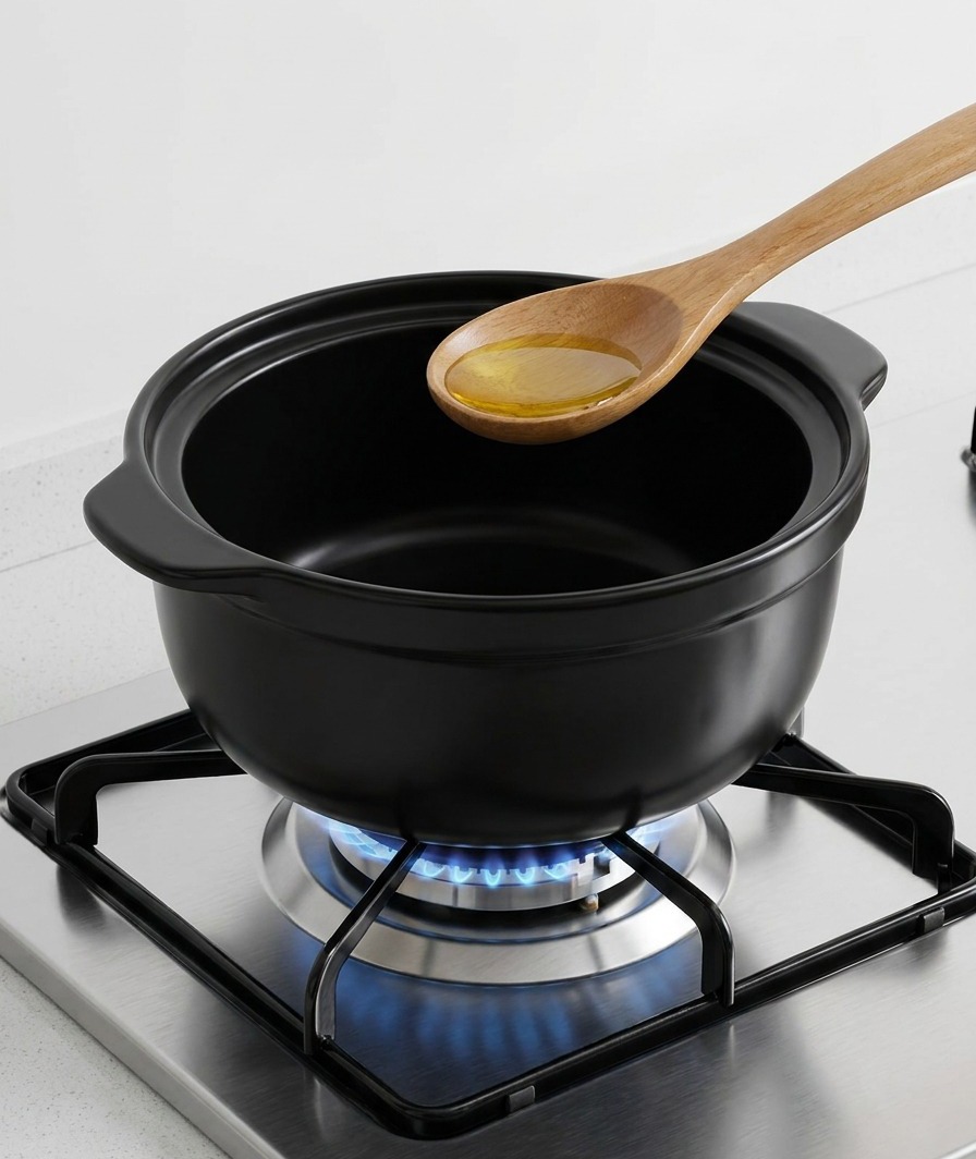 Une cuillère en bois versant de lhuile de sésame dorée au fond dune marmite en céramique noire sur le feu.