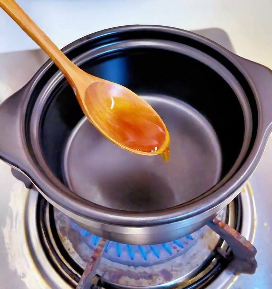 Une cuillère mélangeant des morceaux dail haché dans lhuile au fond dune marmite noire.