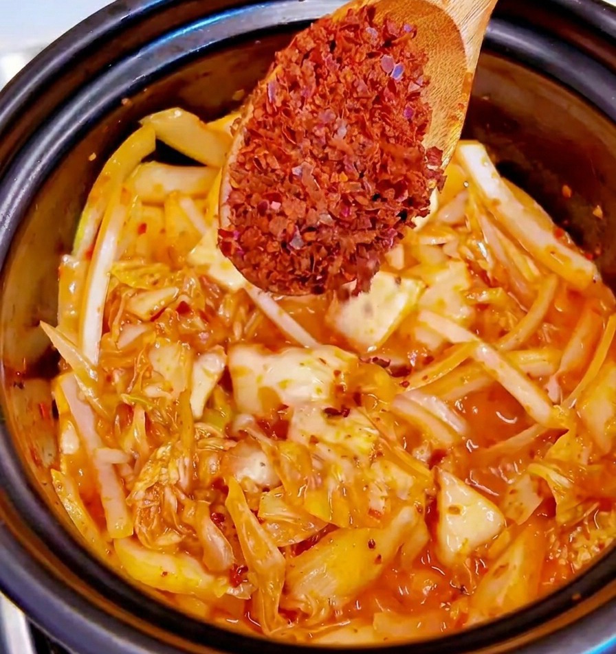 Une cuillère saupoudrant des flocons de piment rouge sur le kimchi et les oignons.