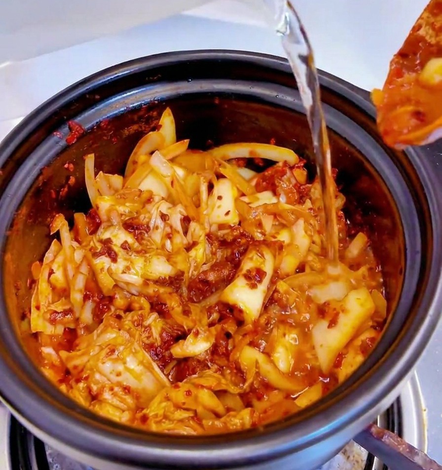 De leau versée dans la marmite noire remplie de la base de kimchi épicée.