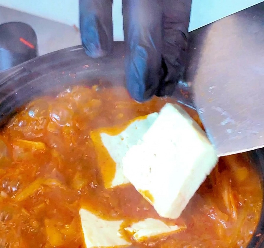 Tranches de tofu blanc déposées délicatement dans la soupe rouge bouillonnante.
