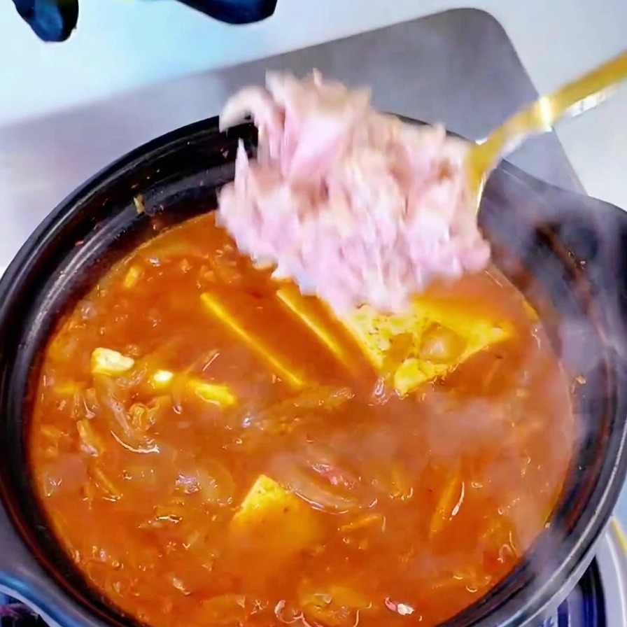 Morceaux de thon ajoutés à la cuillère dans la marmite de soupe.