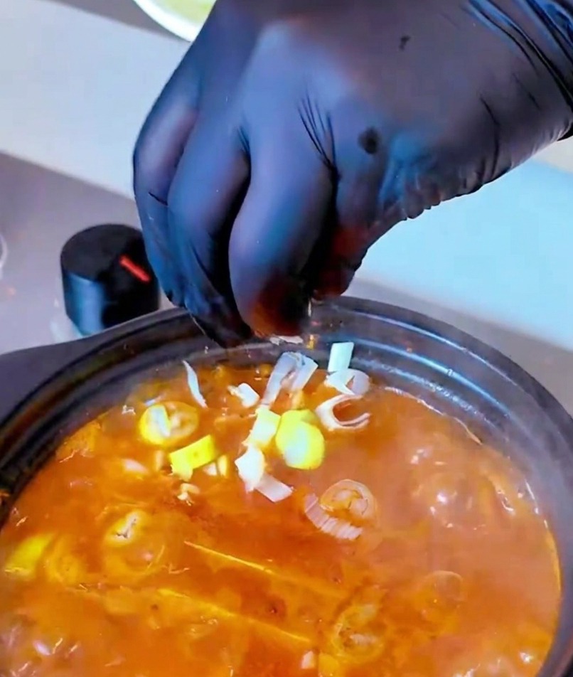 Une main parsemant des oignons verts hachés sur la soupe de kimchi fumante.