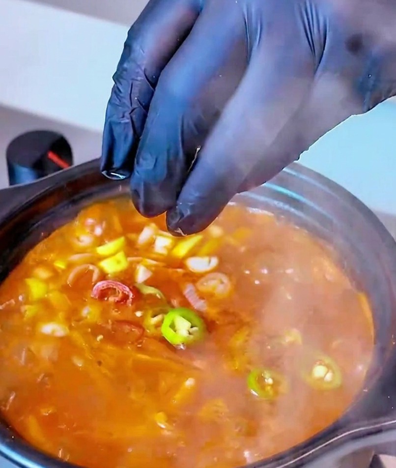Rondelles de piments rouges et verts ajoutées dans la marmite bouillonnante en guise de touche finale.