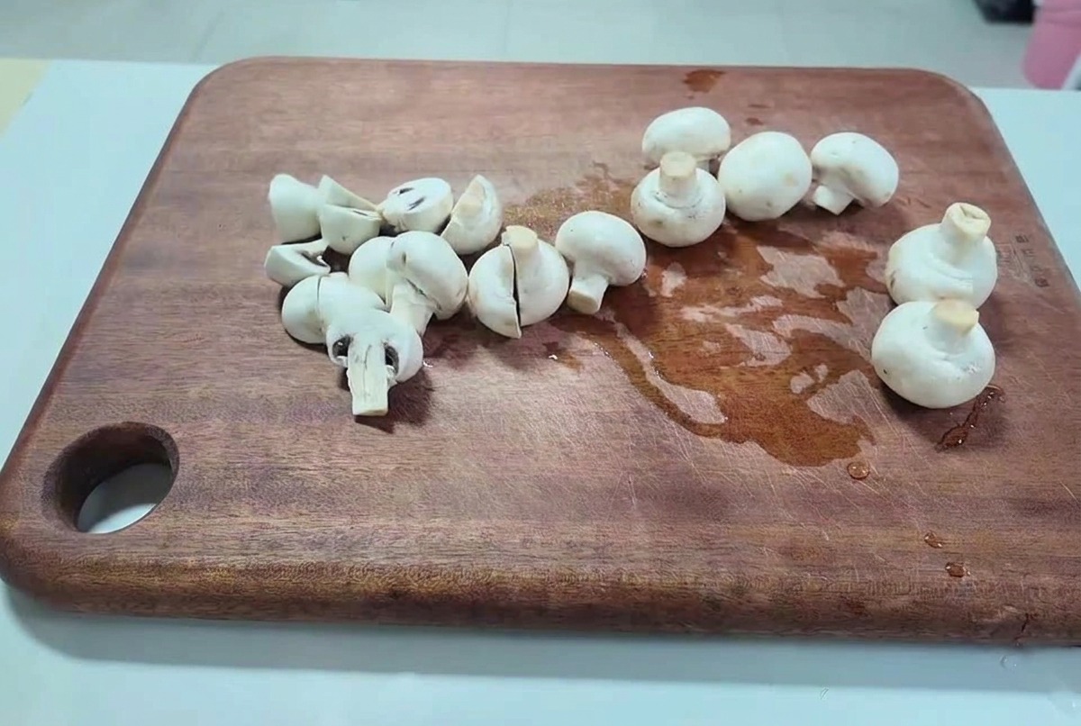Champignons de Paris frais coupés en deux et en morceaux épais sur une planche à découper en bois sombre.