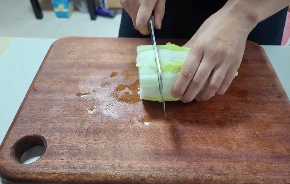 Gros plan sur des mains utilisant un couteau de chef pour hacher des feuilles de chou nappa fraîches.