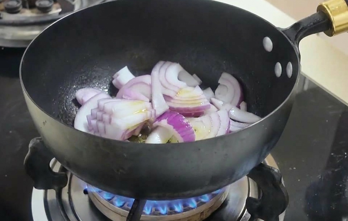 Lamelles doignons rouges sautées dans un wok noir sur une flamme de gaz bleue.