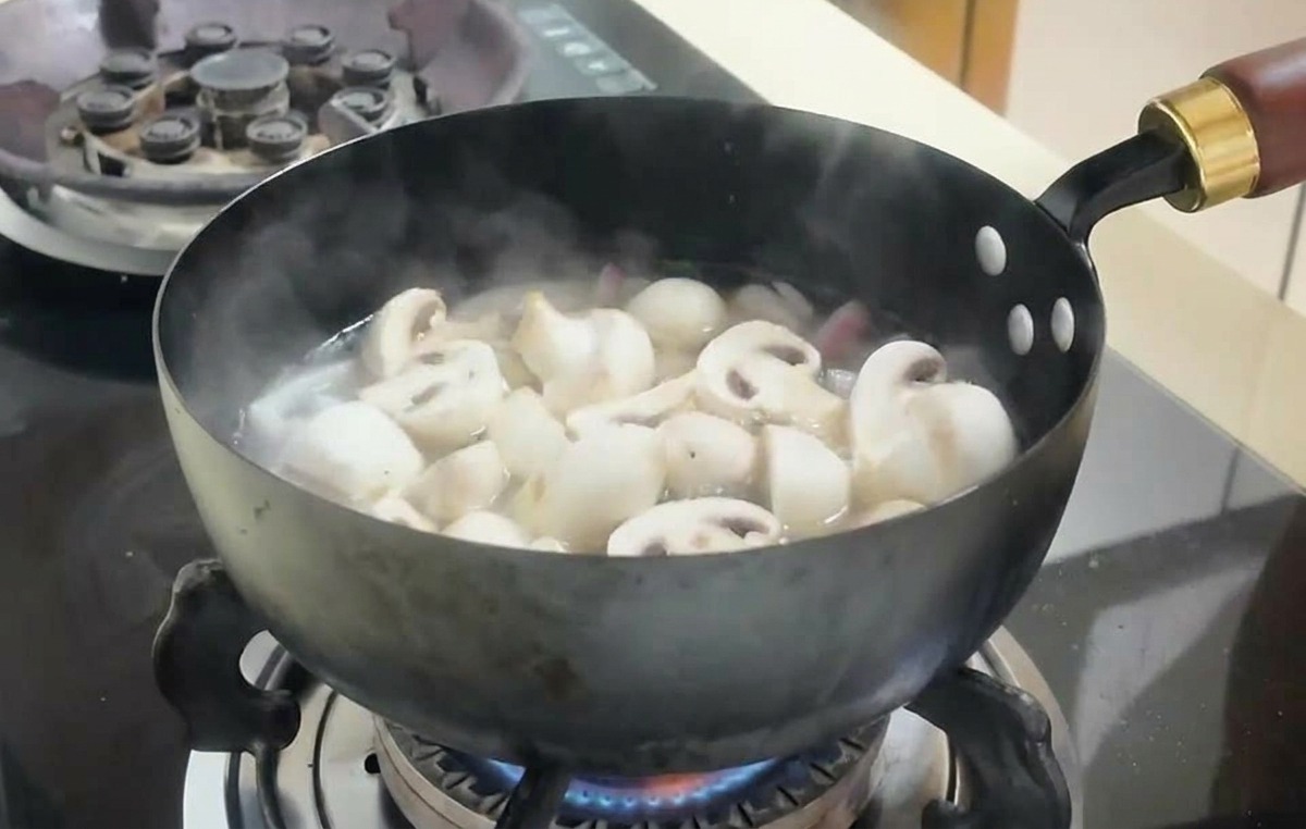 Champignons émincés et cubes de tofu mijotant dans un bouillon bouillonnant dans une poêle sur une cuisinière.