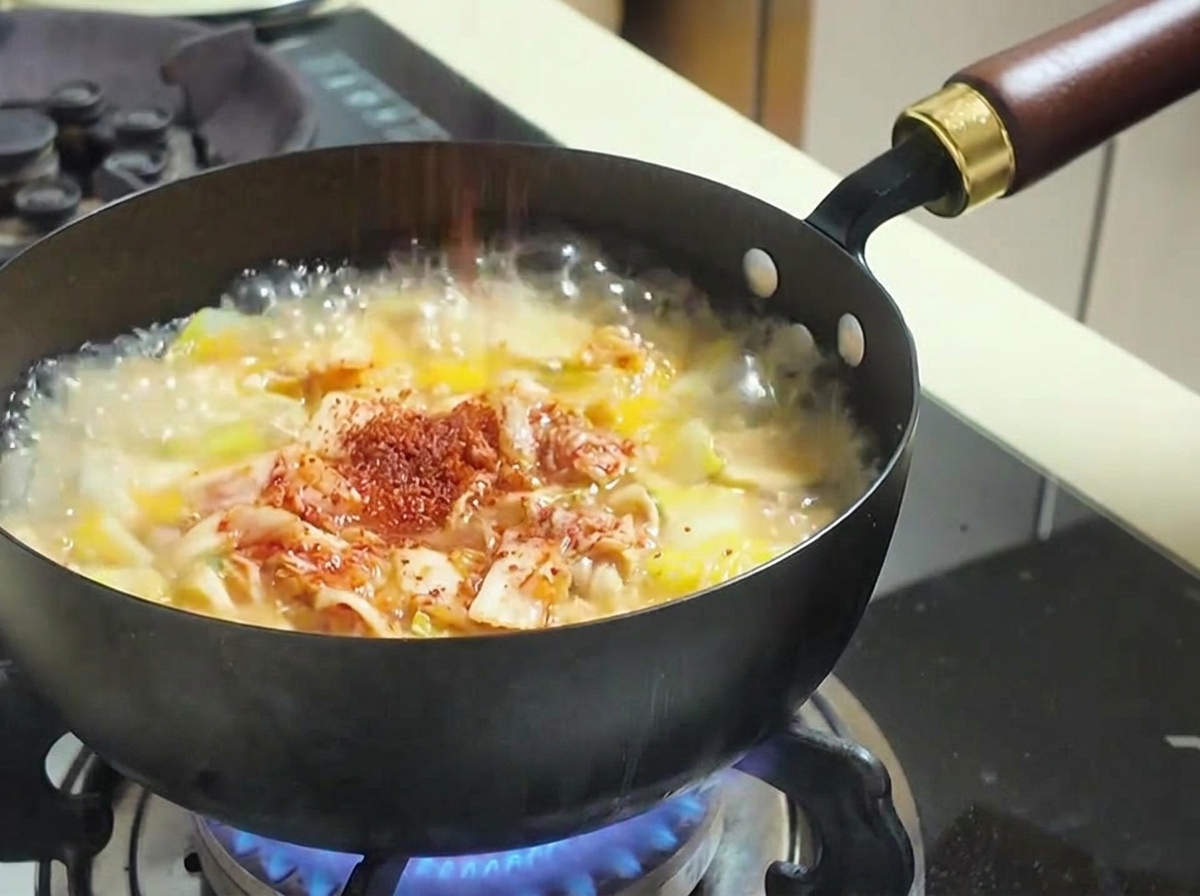 Piment rouge en poudre saupoudré dans une casserole de soupe bouillonnante contenant du kimchi et des légumes.