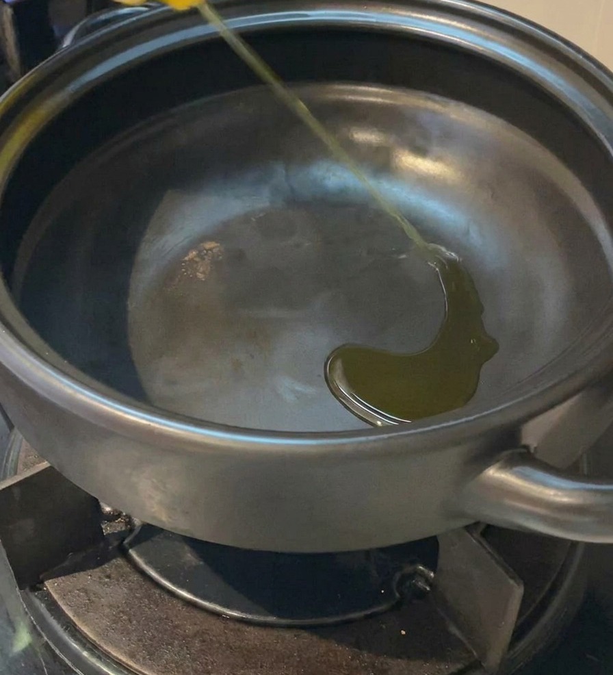 Un fin filet dhuile de cuisson jaune versé au fond dune marmite en terre cuite vide et sombre sur une gazinière.