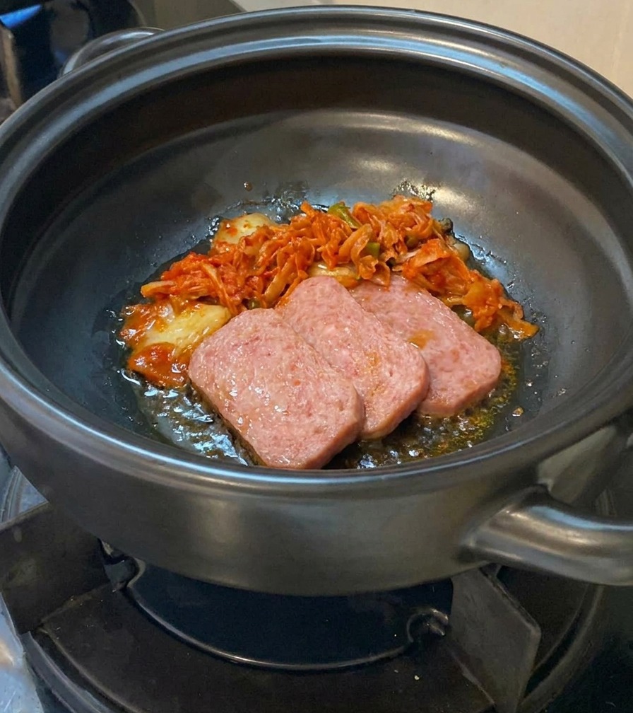 Du kimchi haché ajouté dans une marmite contenant des tranches de viande partiellement cuites.
