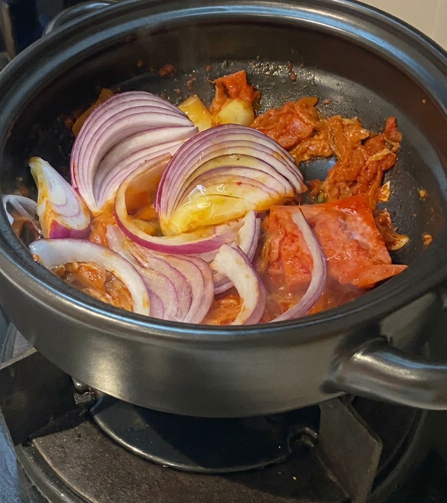 Dépaisses demi-lunes doignon rouge mélangées dans une marmite avec du kimchi et du porc.