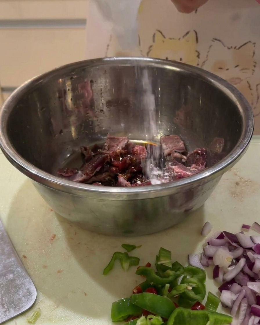 Sauces sombres versées dune bouteille sur des cubes de bœuf crus dans un bol en métal.