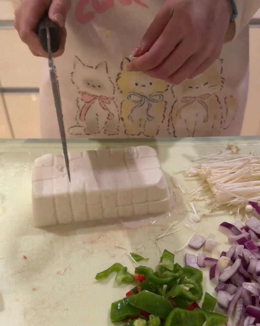 Un bloc de tofu blanc découpé en une grille de petits cubes sur une planche à découper.