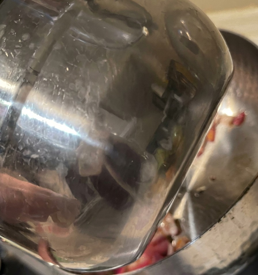 Eau versée dune tasse en inox dans une marmite contenant les oignons rouges sautés.
