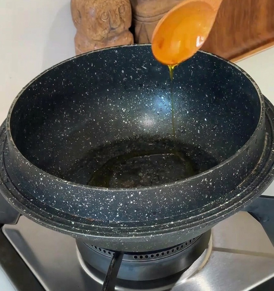 Huile de cuisson versée dune cuillère en bois clair dans un pot en pierre moucheté sur une cuisinière moderne.