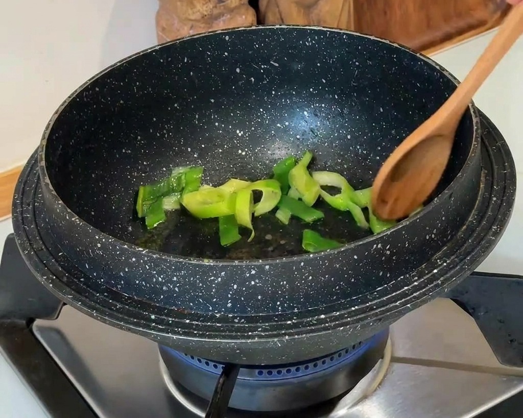 Oignons verts hachés remués avec une cuillère en bois dans un pot noir à motif granit sur une cuisinière à gaz.