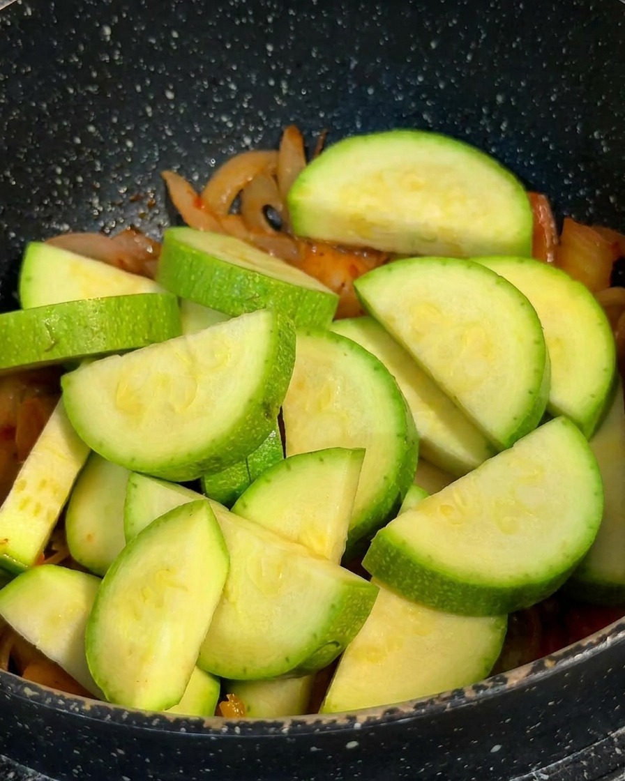 Épaisses tranches de courgette verte en demi-lune empilées dans un pot sur une base de kimchi et doignons cuits.