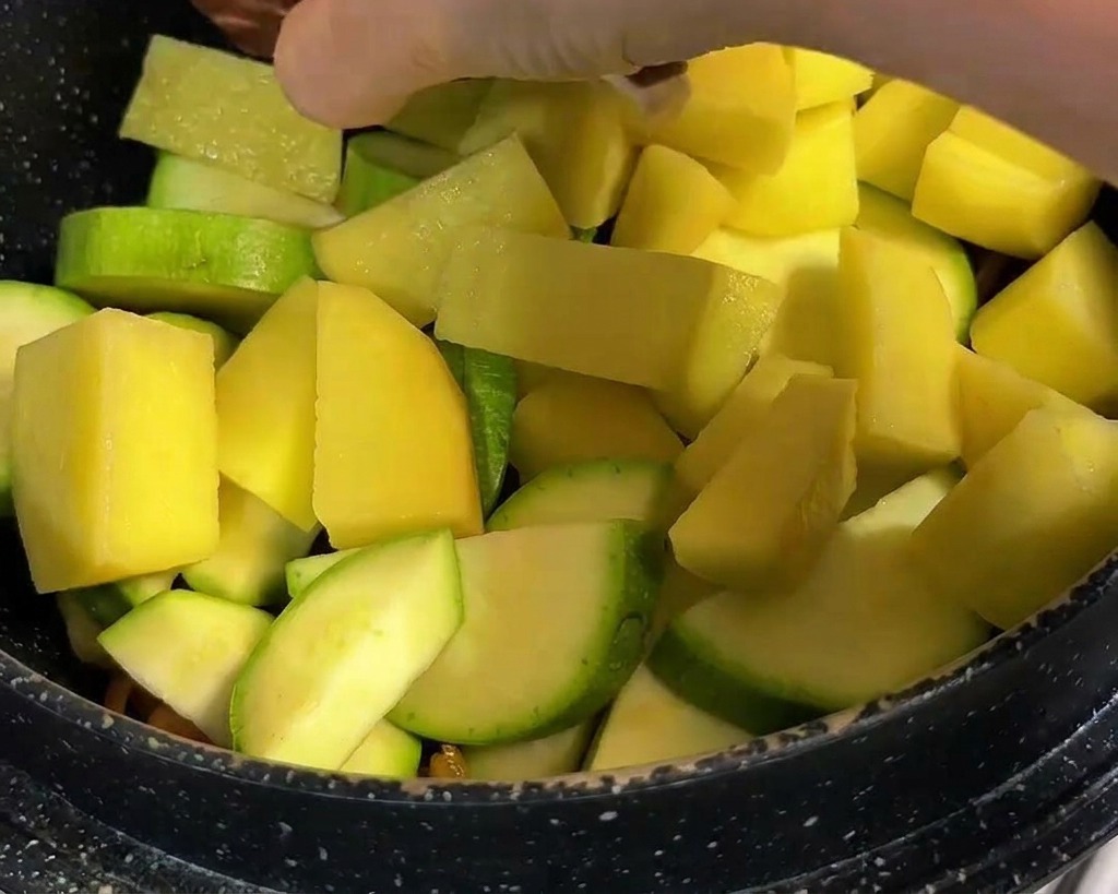 Morceaux de pomme de terre jaune et shiitakés entiers incisés ajoutés à un pot de légumes.