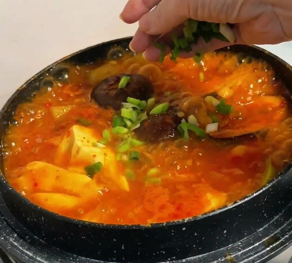 Oignons verts hachés parsemés à la main sur un ragoût coréen bouillonnant contenant du tofu et des champignons.