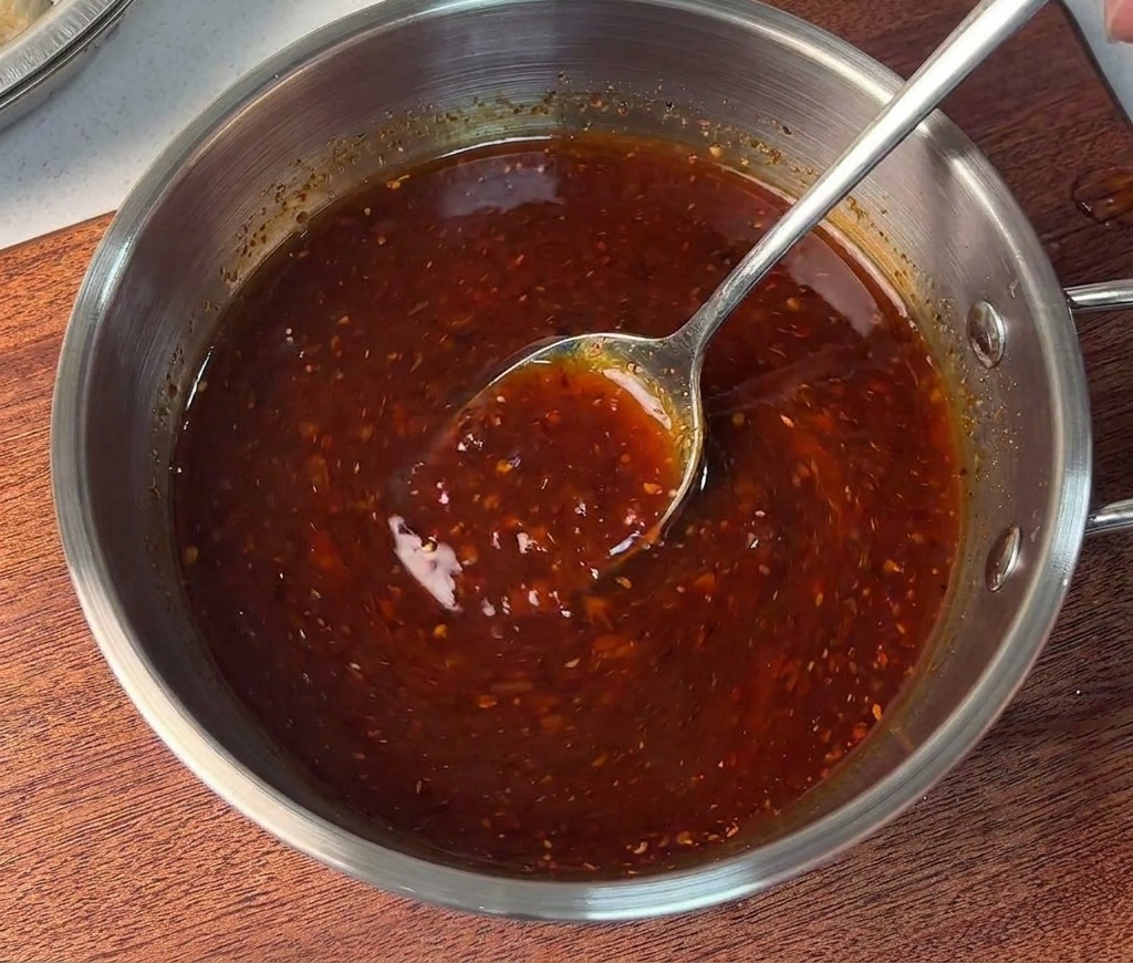 Une personne mélangeant une sauce rouge épaisse et vibrante dans un petit bol en inox.