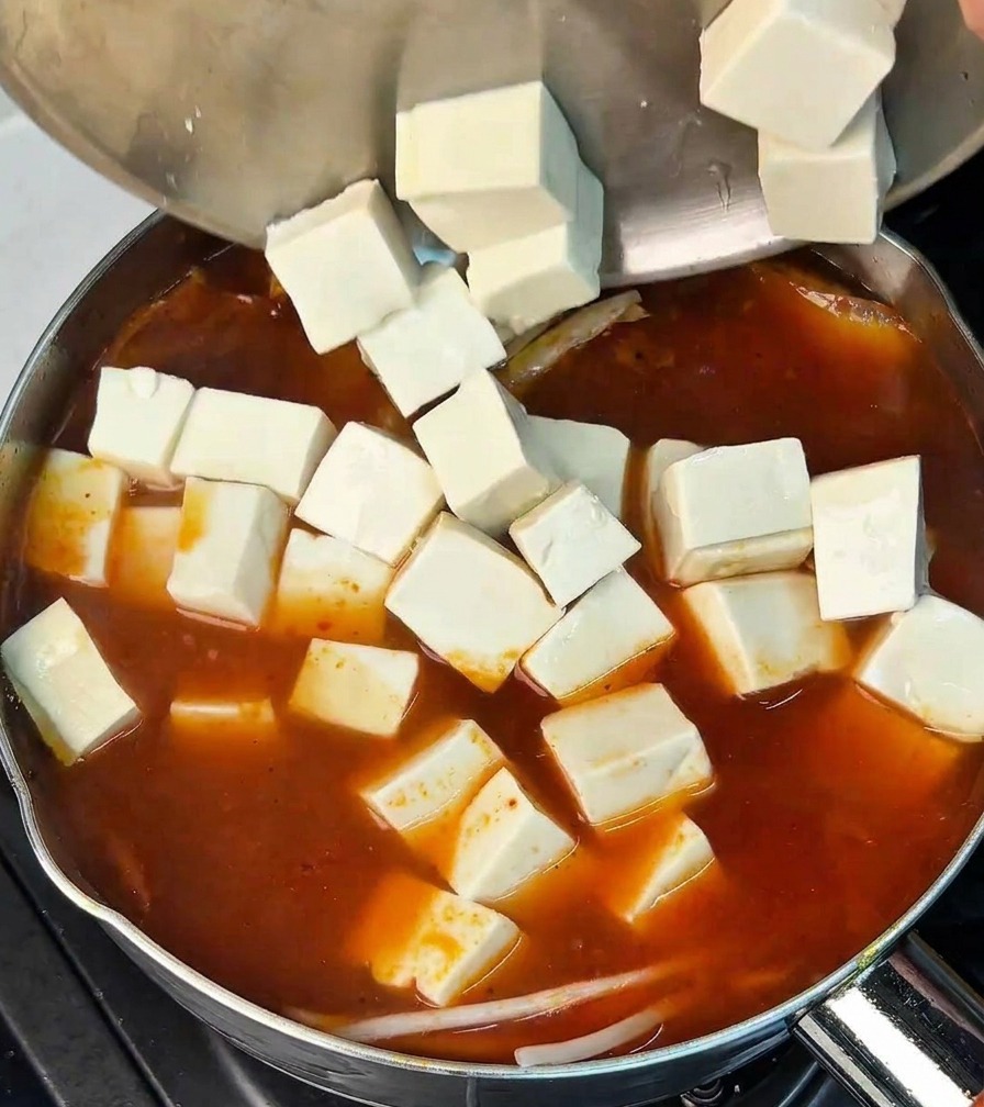 Cubes de tofu blanc versés dun bol en inox dans le bouillon de kimchi bouillonnant.