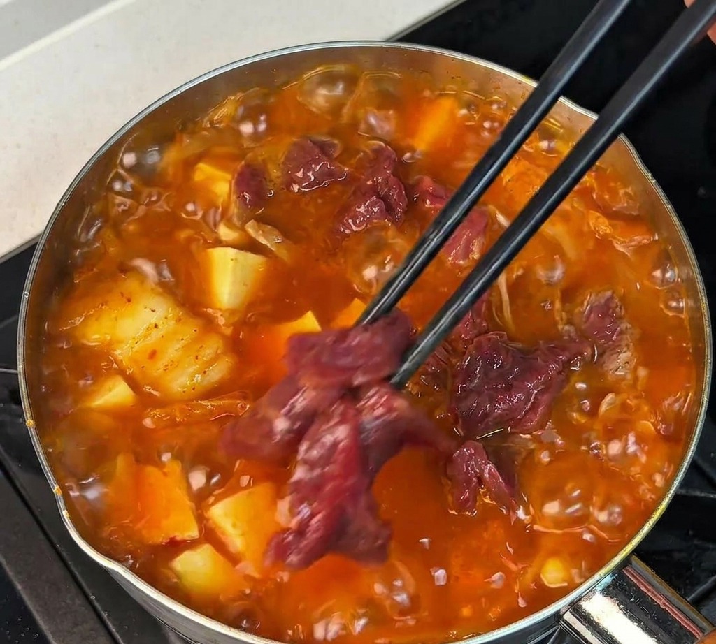 Tranches de bœuf cru mariné déposées dans la soupe rouge avec des baguettes noires.