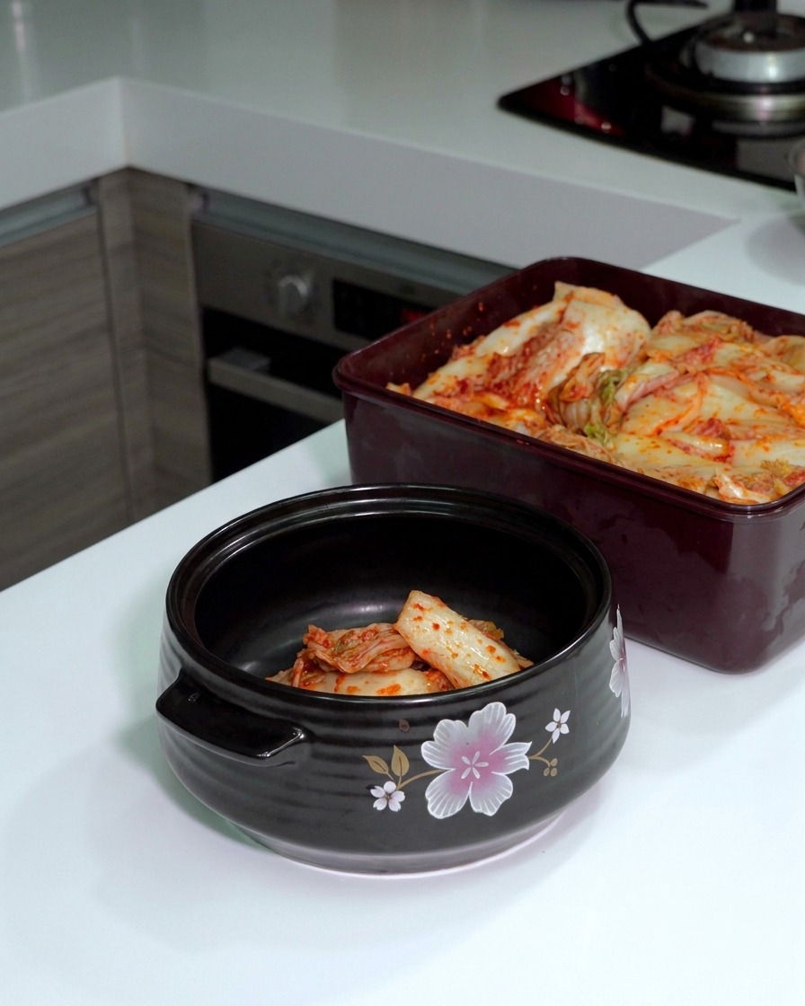 Du kimchi de chou fermenté coupé avec des ciseaux argentés directement dans une marmite en céramique noire.