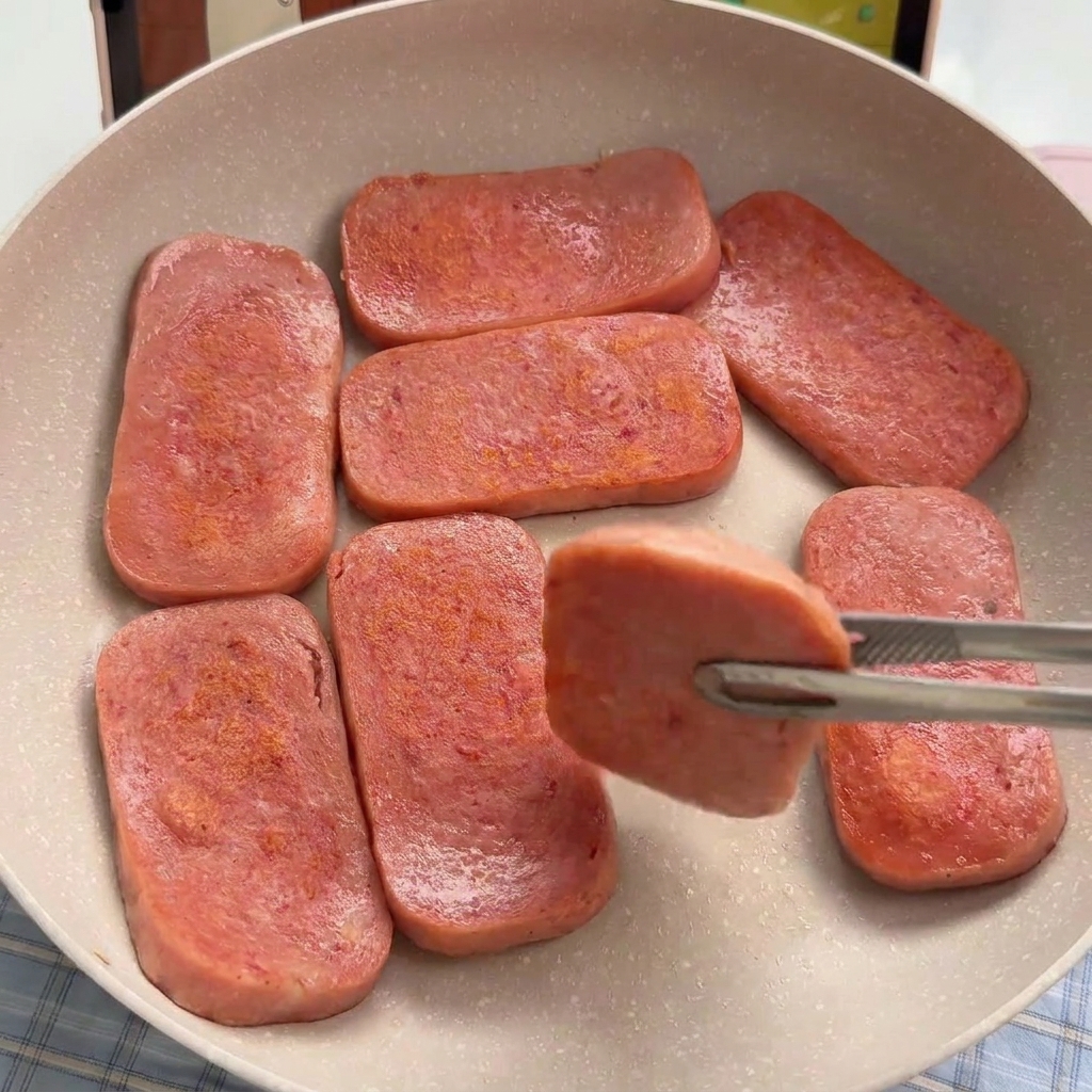Tranches de jambon en conserve en train de dorer dans une poêle antiadhésive.