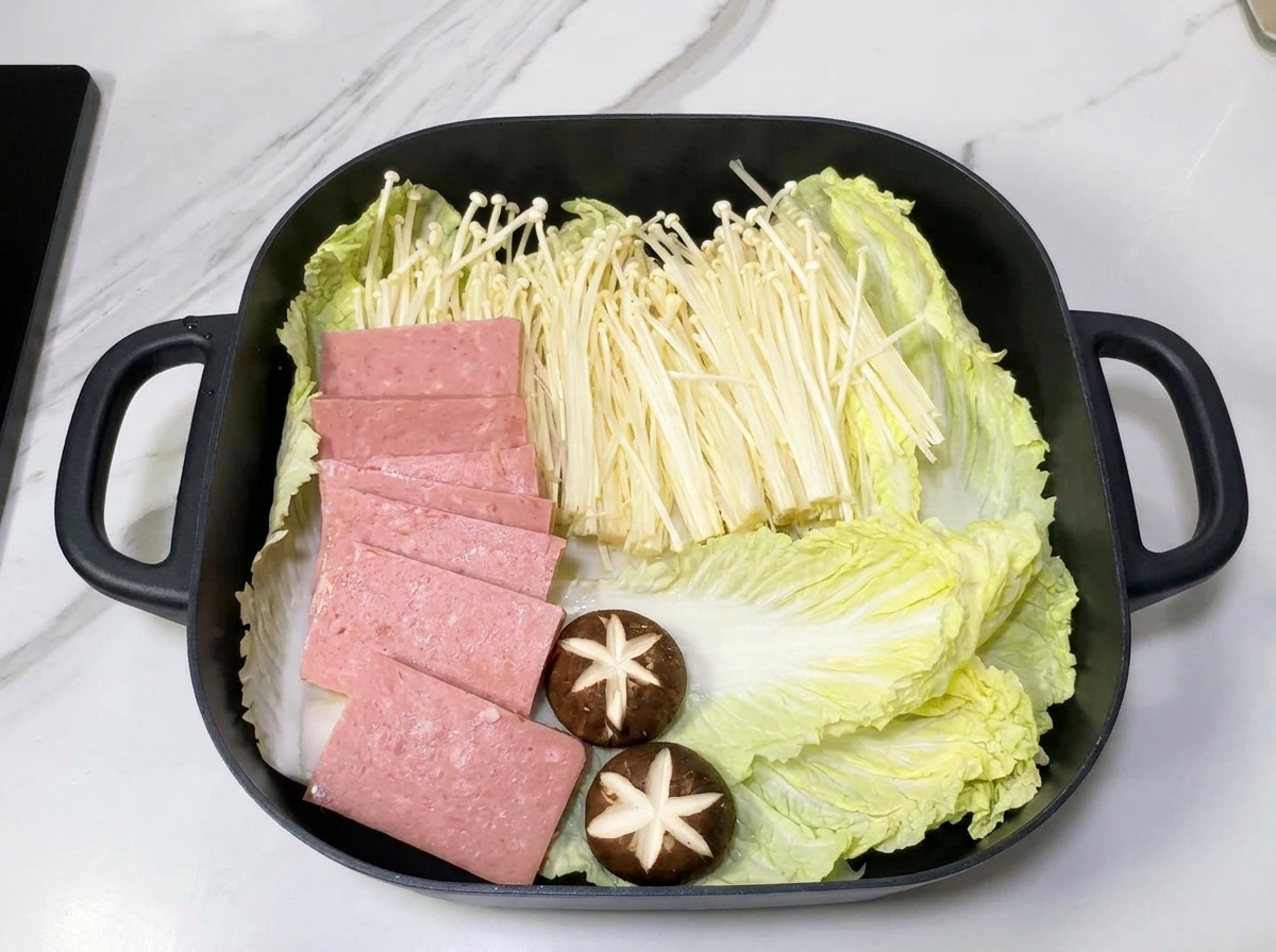 Marmite contenant des couches de chou chinois, de champignons enoki et de tranches de Spam sur un lit doignons.