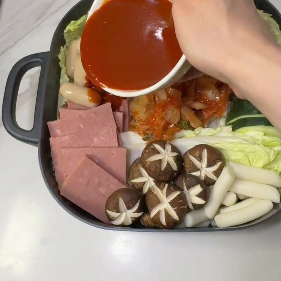 Sauce rouge au gochujang versée au centre des ingrédients crus du ragoût de larmée.