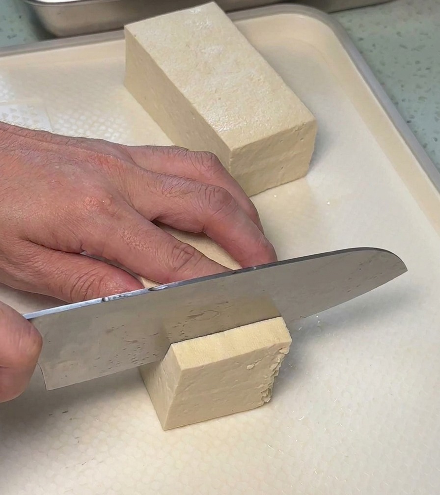 Découpe dun bloc de tofu ferme en tranches rectangulaires sur une planche à découper blanche.