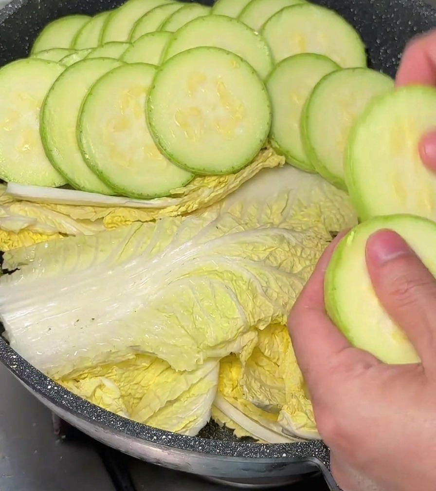 Mains plaçant soigneusement des rondelles de courgettes en rosace dans la marmite tapissée de chou.